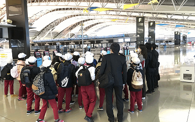 空港のチェックインカウンターを見学する小学生の写真