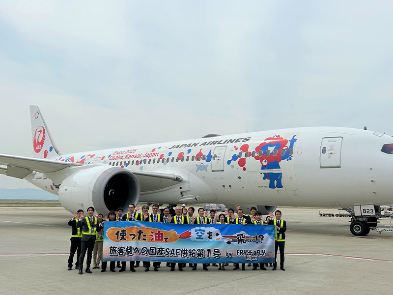 Personnel taking a commemorative photo in front of an airplane, holding a banner that reads “Flying in the sky using used oil!”