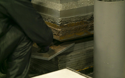 作業員が、高さ調整用の鉄板を一枚ずつ手で慎重に挿入している様子の手元のクローズアップ写真。