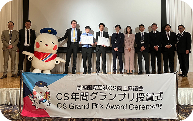 「関西国際空港CS向上協議会 CS年間グランプリ授賞式」と書かれた横断幕の前で撮影された記念写真。