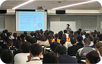 多くの空港スタッフの前で外部講師がお客さま満足向上に係る講演会を実施している様子の写真。