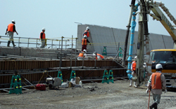 Several workers are building a concrete wall on an embankment construction site.