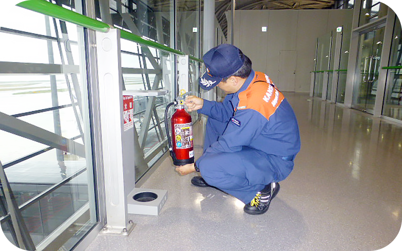 A staff member conducts a safety check on fire extinguishers inside an airport terminal building.